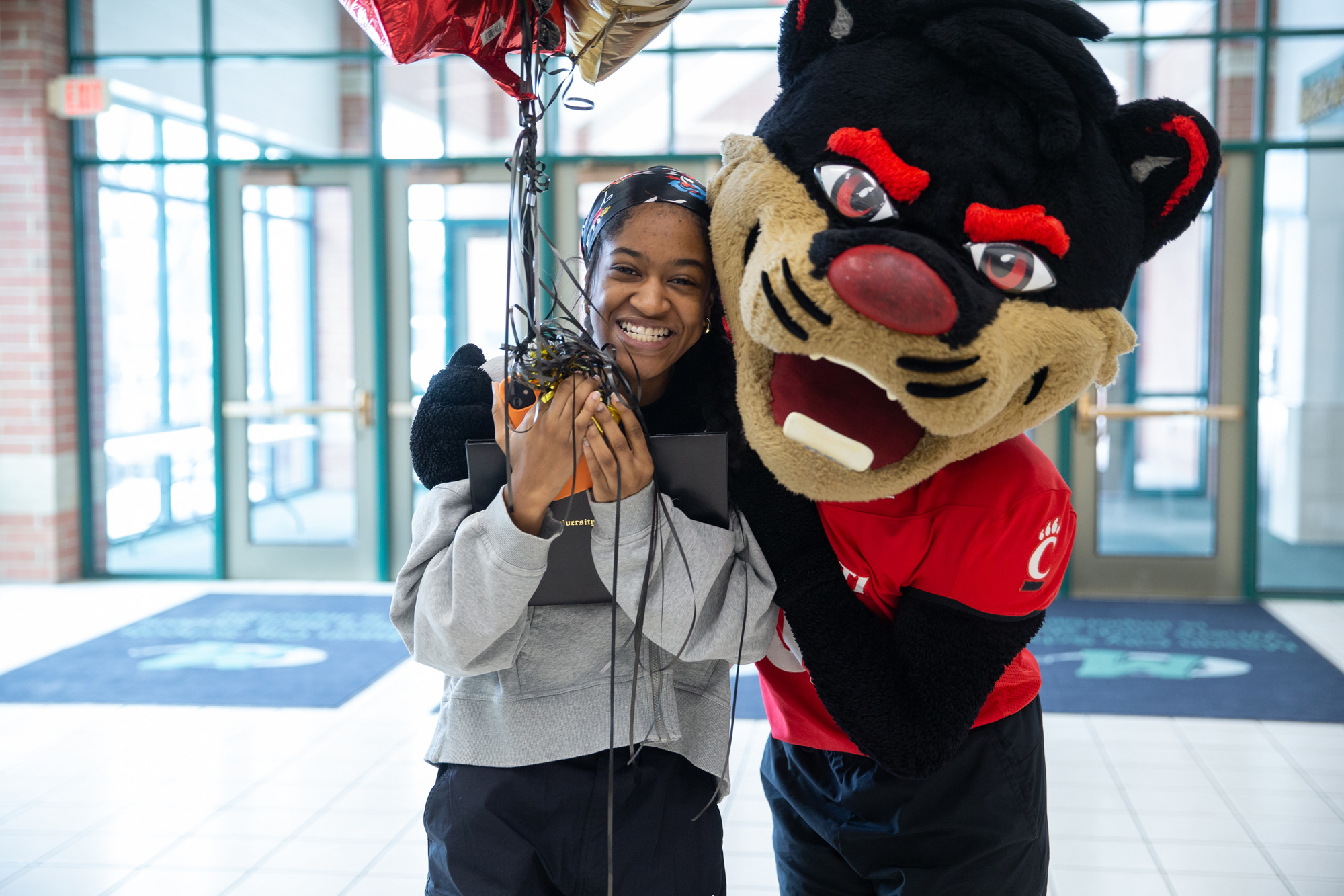 A student recently admitted to UC holds balloons and poses with the Bearcat Mascot 